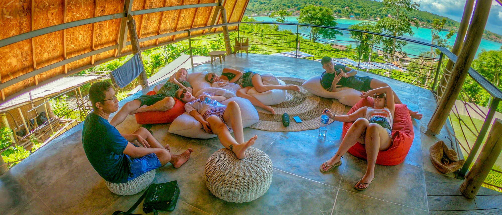 Group of travelers relaxing on bean bags on a hillside deck overlooking teal water in Nusa Lembongan.