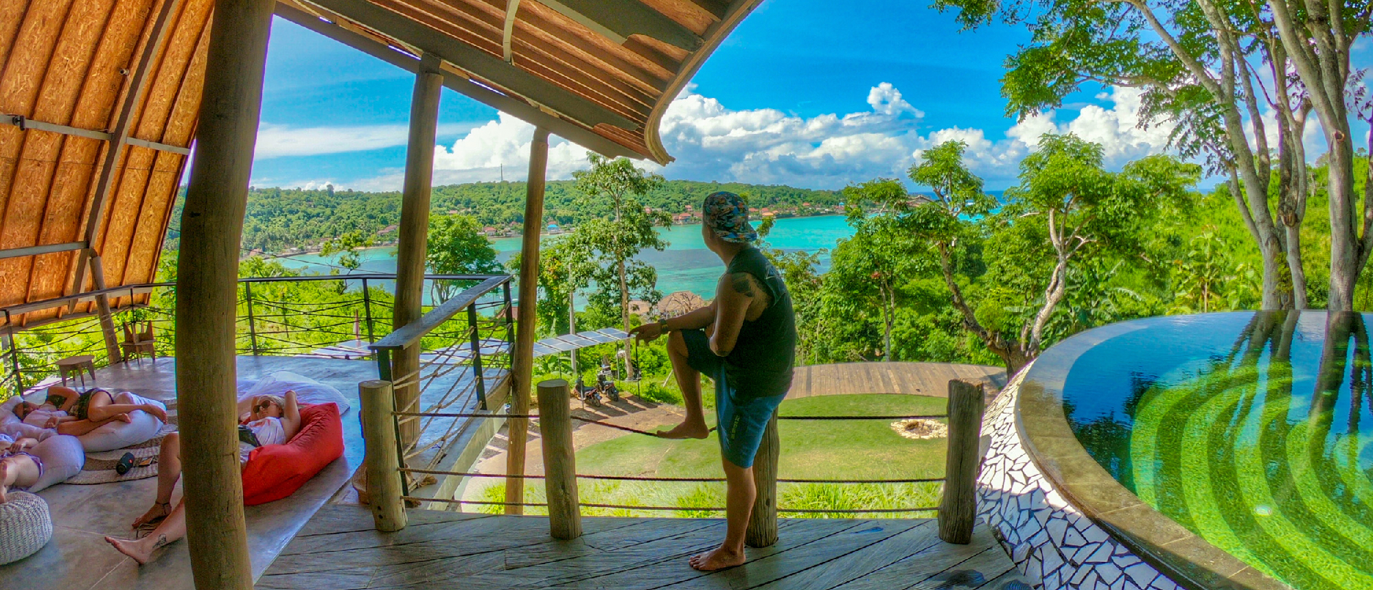 People relax on a hillside deck, enjoying the stunning turquoise waters and lush islands of Nusa Lembongan.