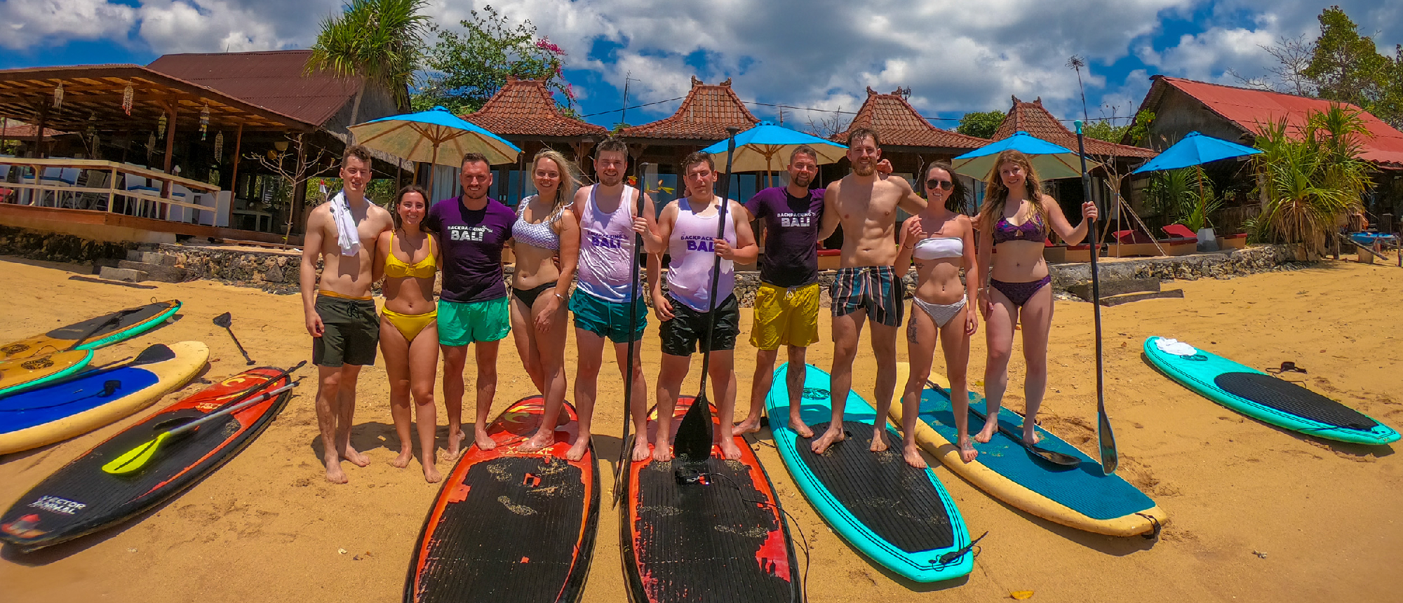 A group of happy backpackers with stand-up paddleboards on a tropical beach in Nusa Lembongan.