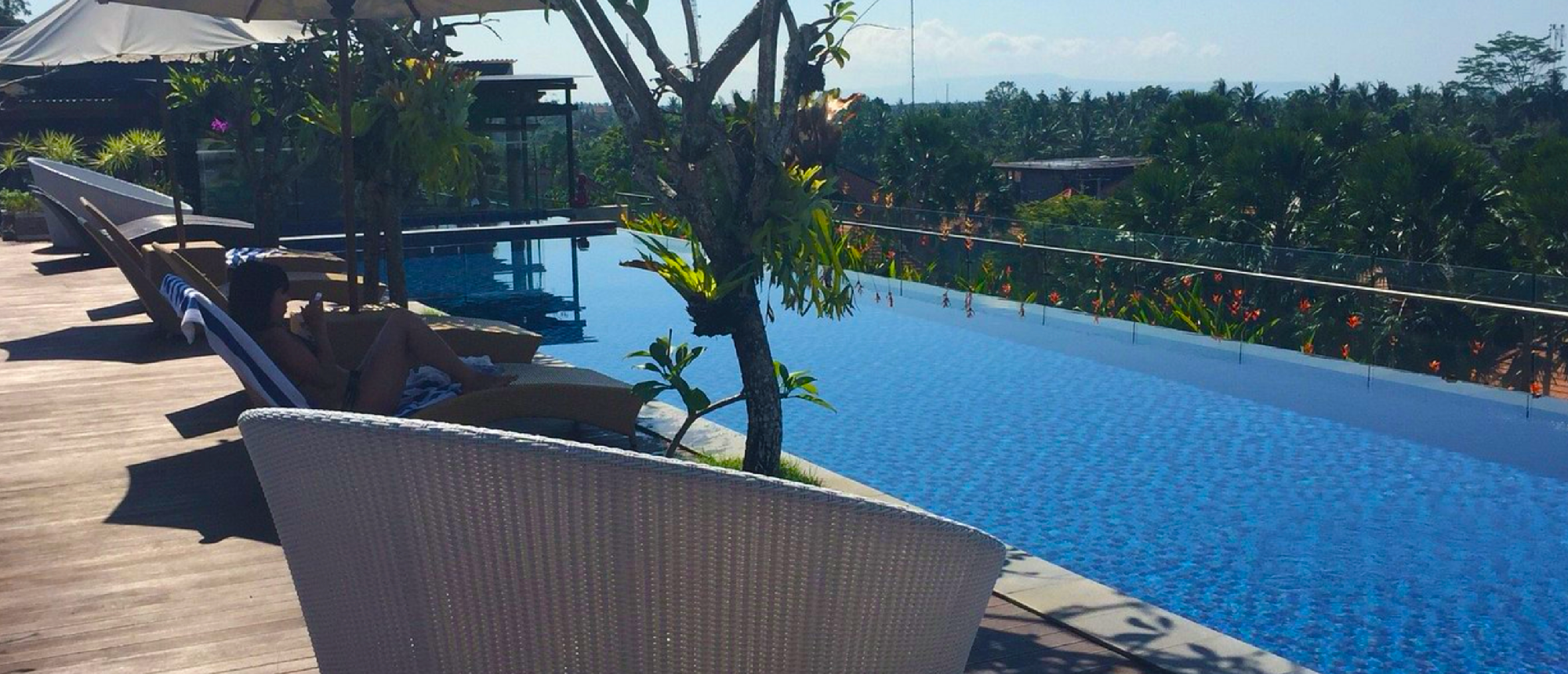 A person lounges by a stunning infinity pool with a panoramic view of the lush Ubud jungle.