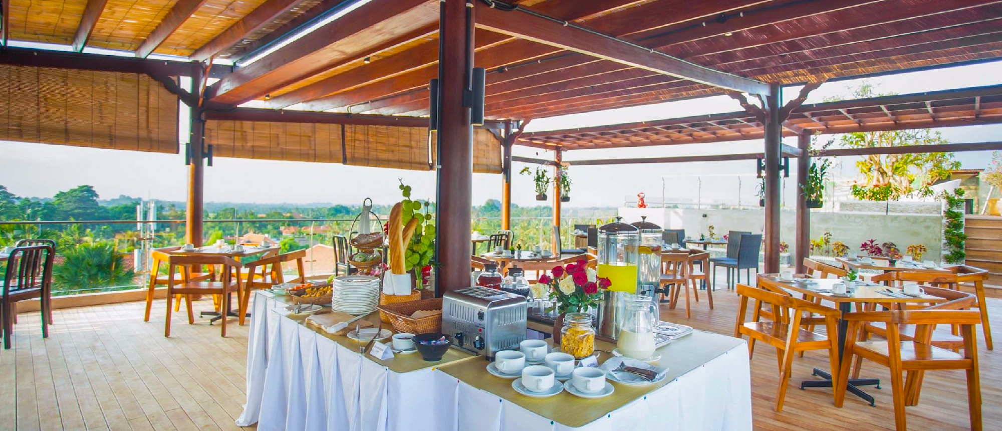An outdoor restaurant with a breakfast buffet and wooden tables overlooking a green landscape in Ubud.