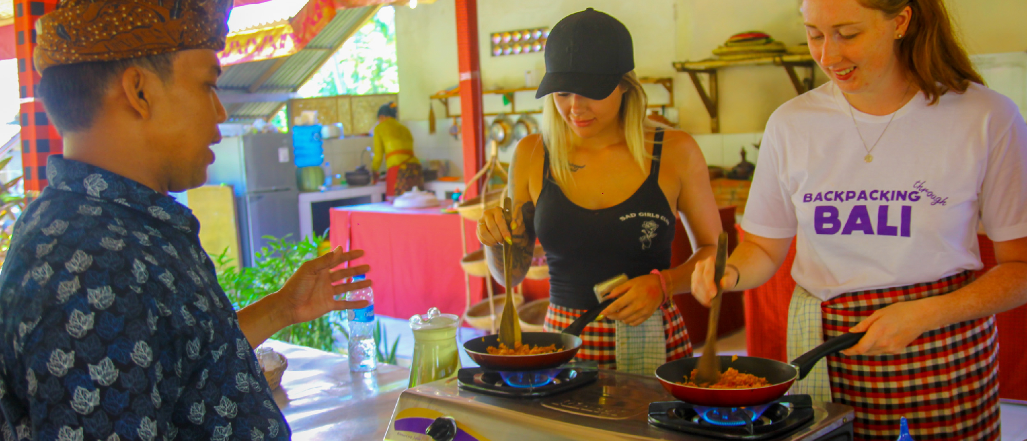 A local Balinese man teaches two women to cook traditional dishes in an outdoor kitchen in Ubud.