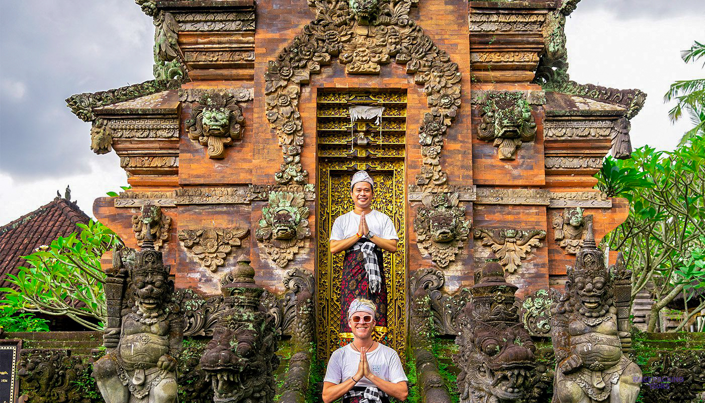 Two men in traditional Balinese dress pose at a beautifully carved ancient temple in Canggu.