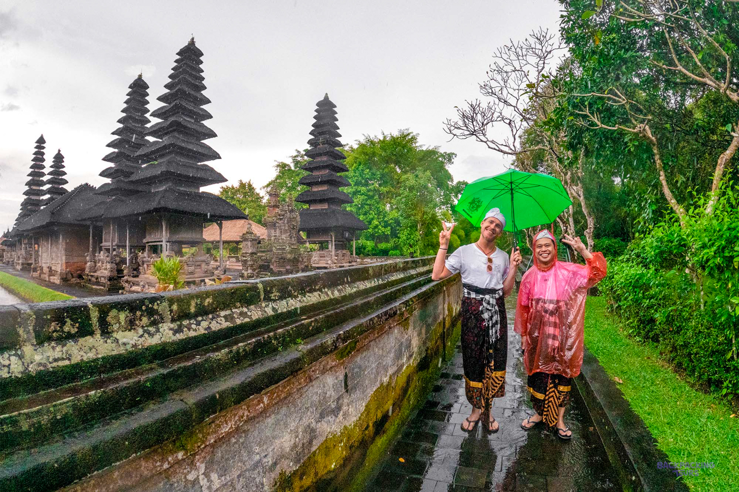 Backpackers smile and make peace signs in the rain at a beautiful Balinese temple.