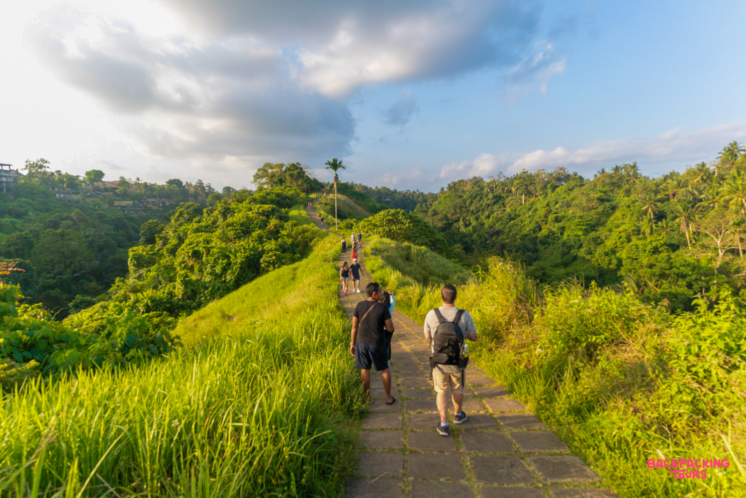 Travelers walk a beautiful paved path through vibrant green hills and tropical jungle in Ubud.