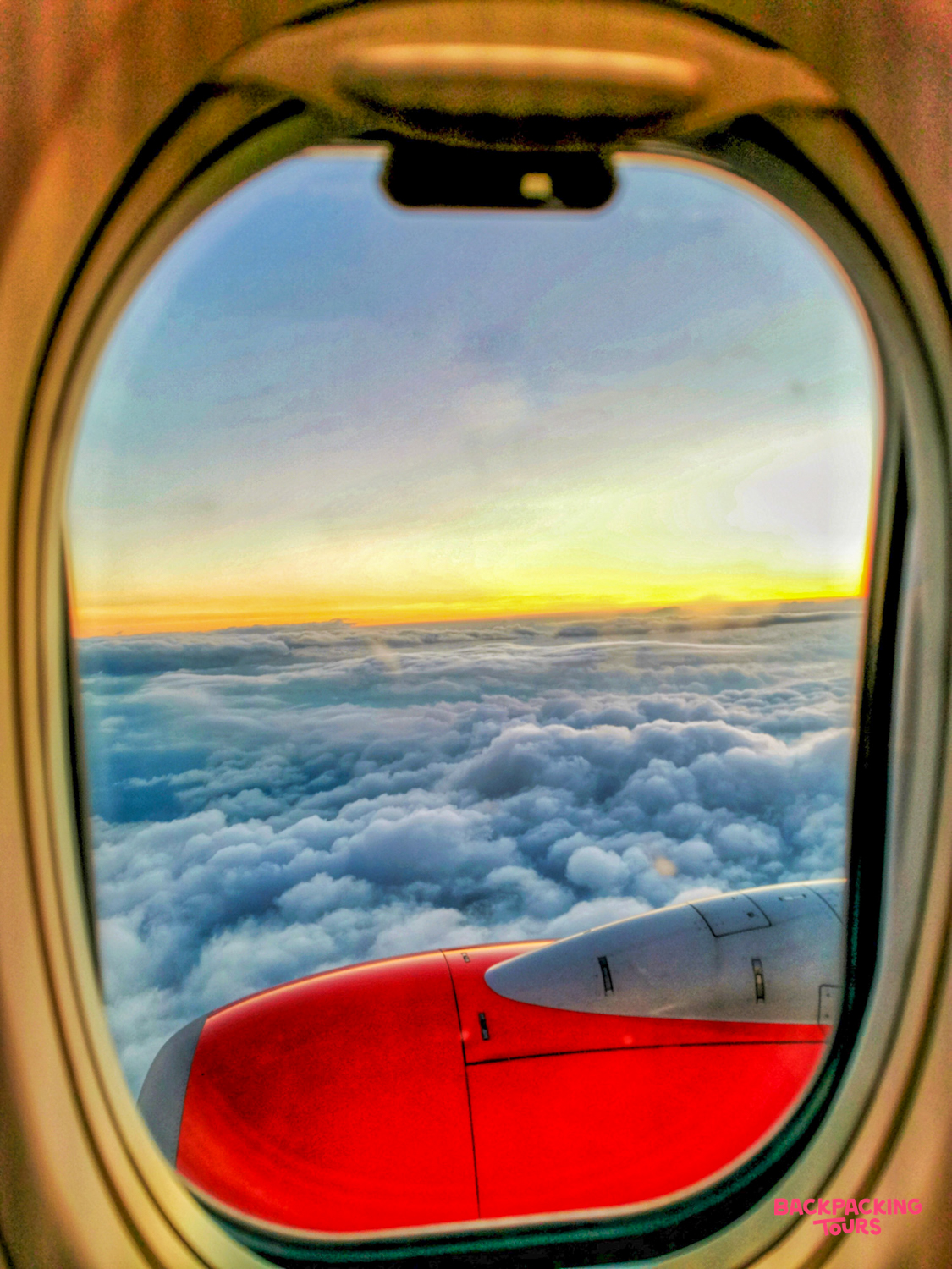 A stunning sunset view from an airplane window, flying high above fluffy clouds on the way to Bali.