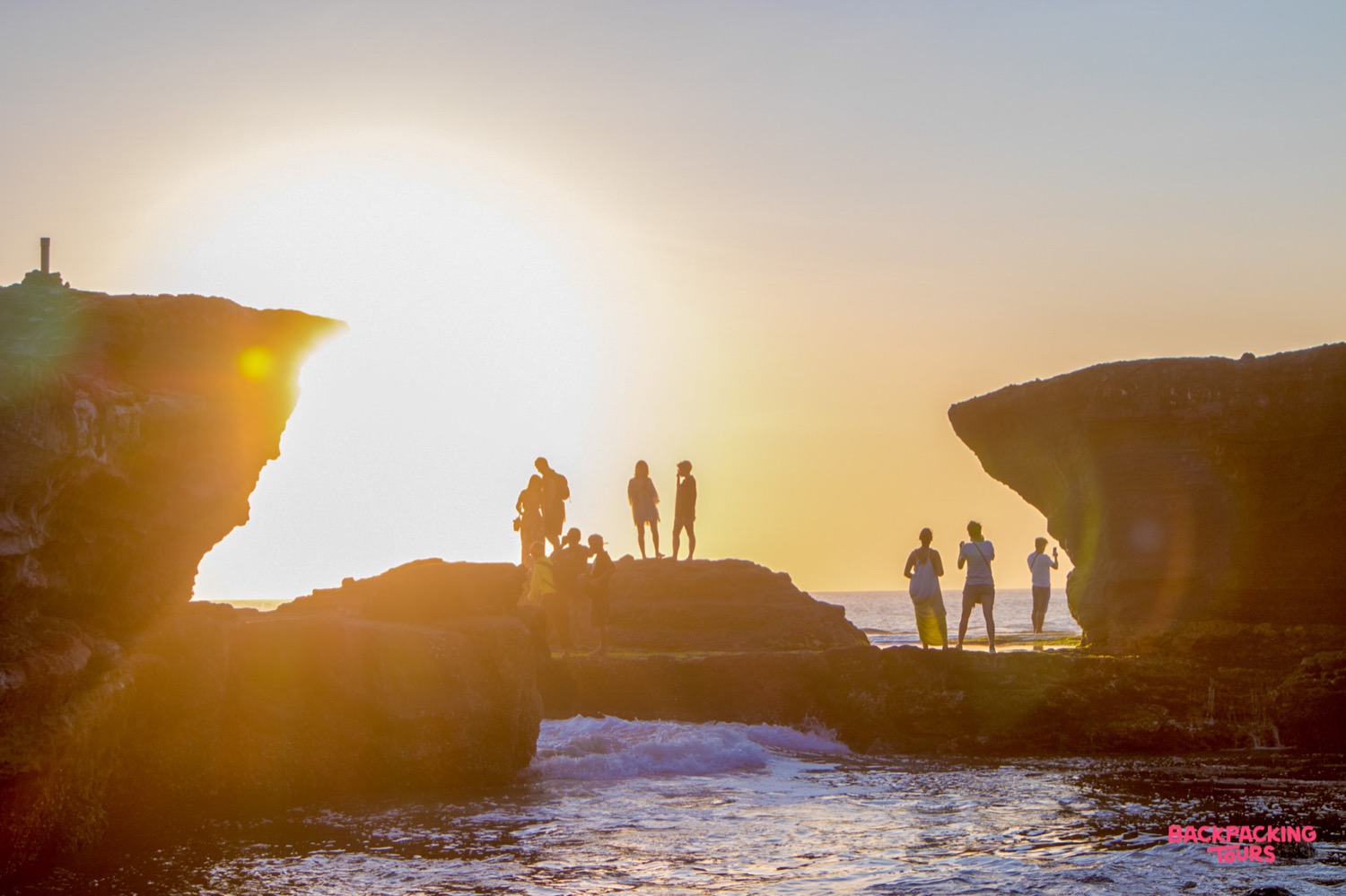 Travelers enjoy a beautiful golden sunset over the rocky coastline of Kuta, Bali.