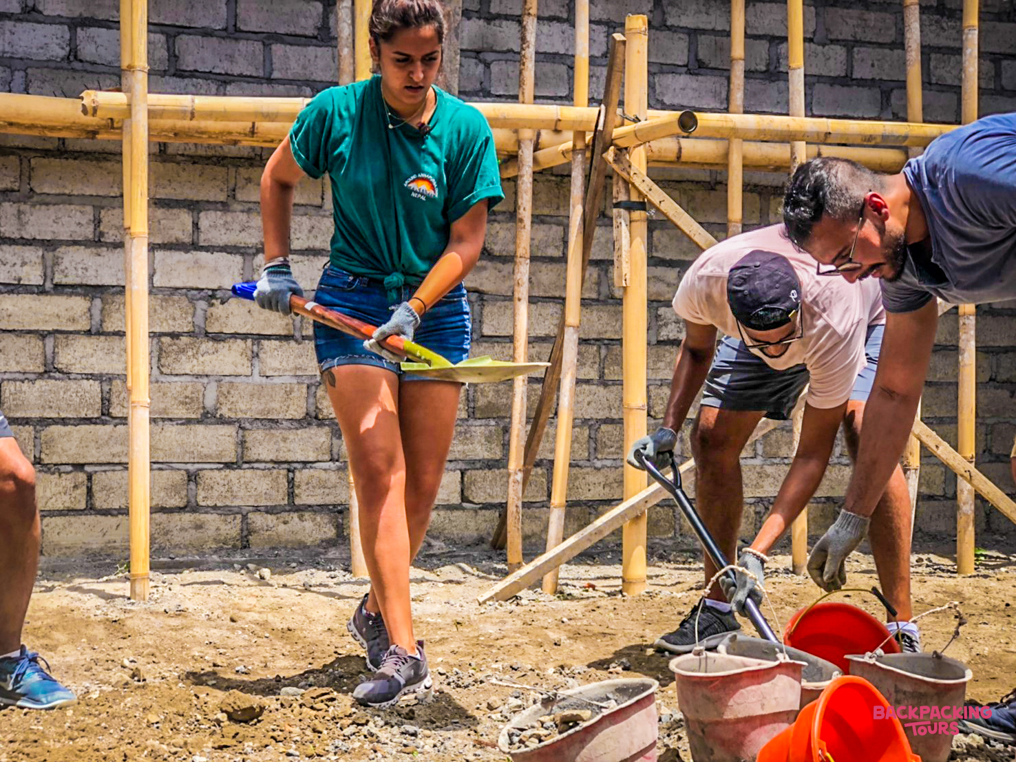 Volunteers work together on a construction site in Bali, mixing materials and leveling ground.