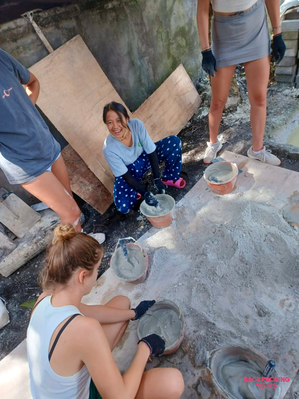 Smiling volunteers work together mixing cement and building materials at a construction site in Bali.