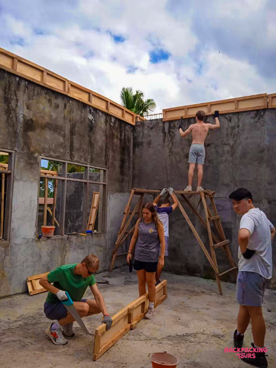 Young volunteers actively building and renovating a house, sawing wood and installing frames on walls in Bali.