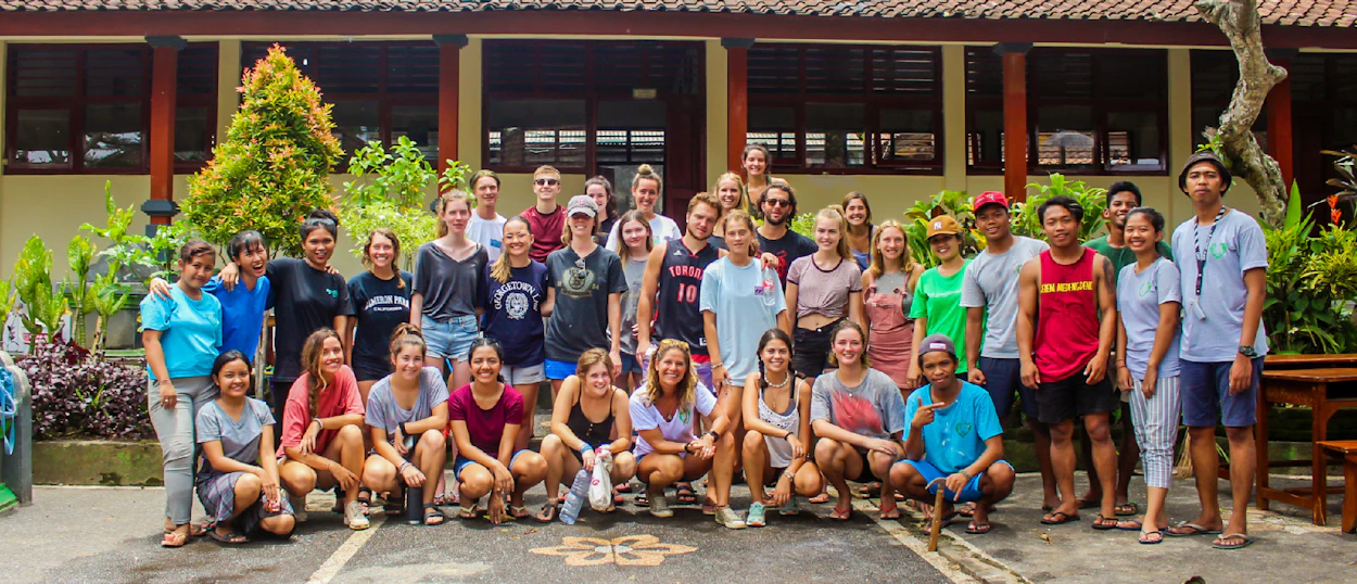 A large group of smiling international volunteers and local community members posing in front of a building in Bali.