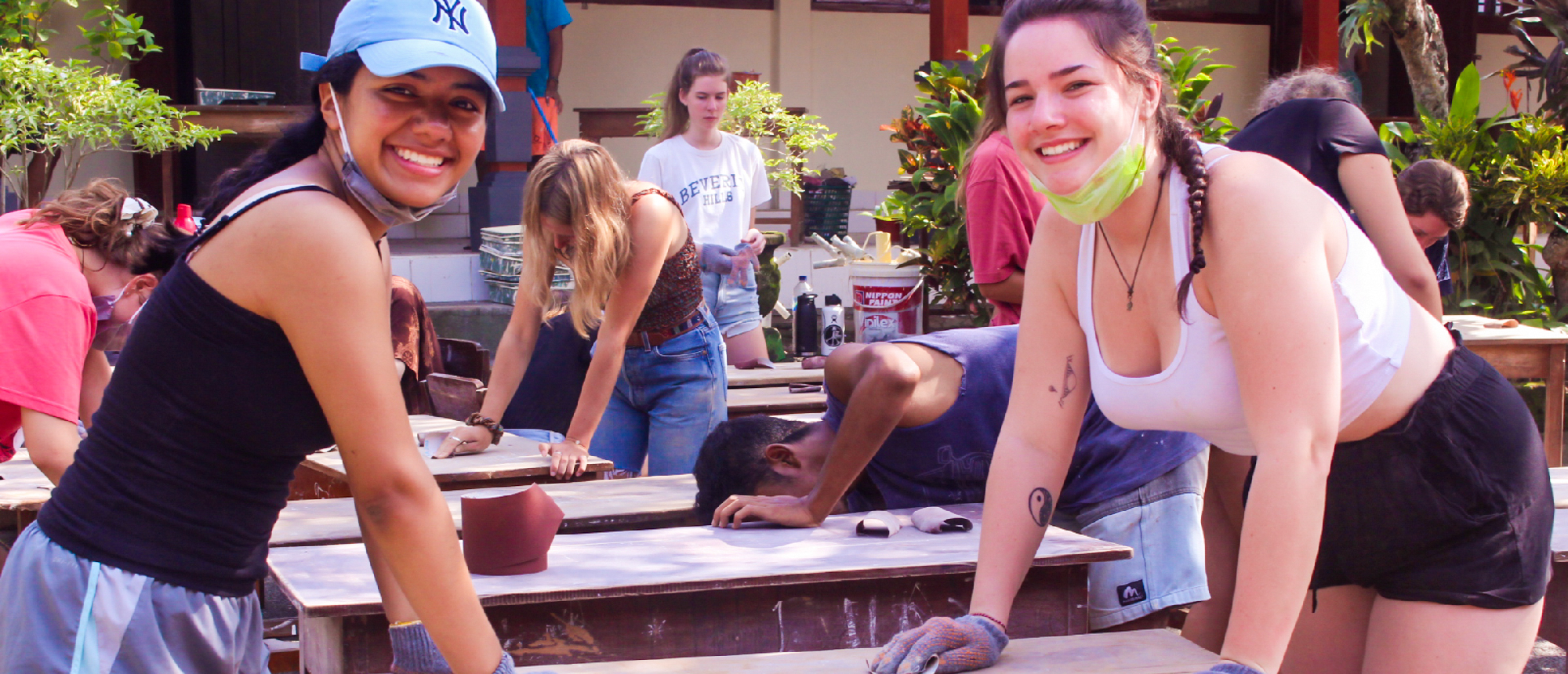 Happy volunteers sanding wooden surfaces during an outdoor community renovation project.