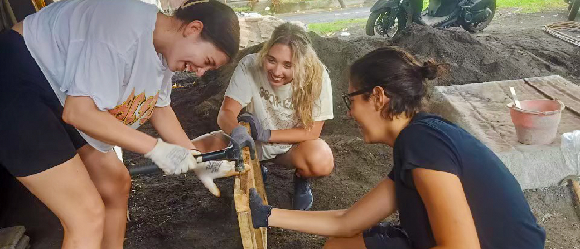Three happy women working together on a construction project, mixing materials and laughing.