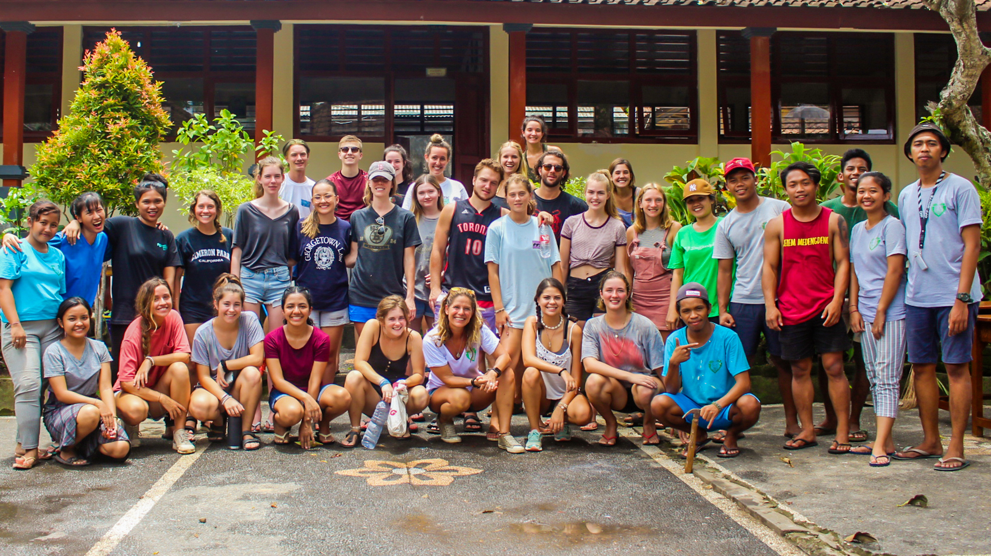 A large, diverse group of smiling volunteers and local people pose for a photo in Bali.