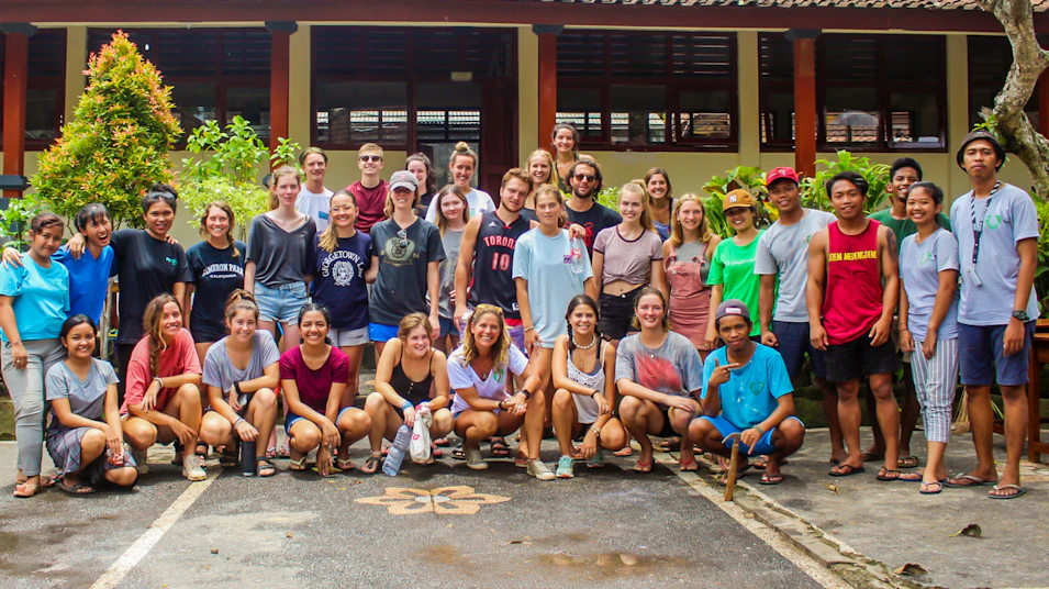 A large, diverse group of smiling volunteers and local people pose for a photo in Bali.