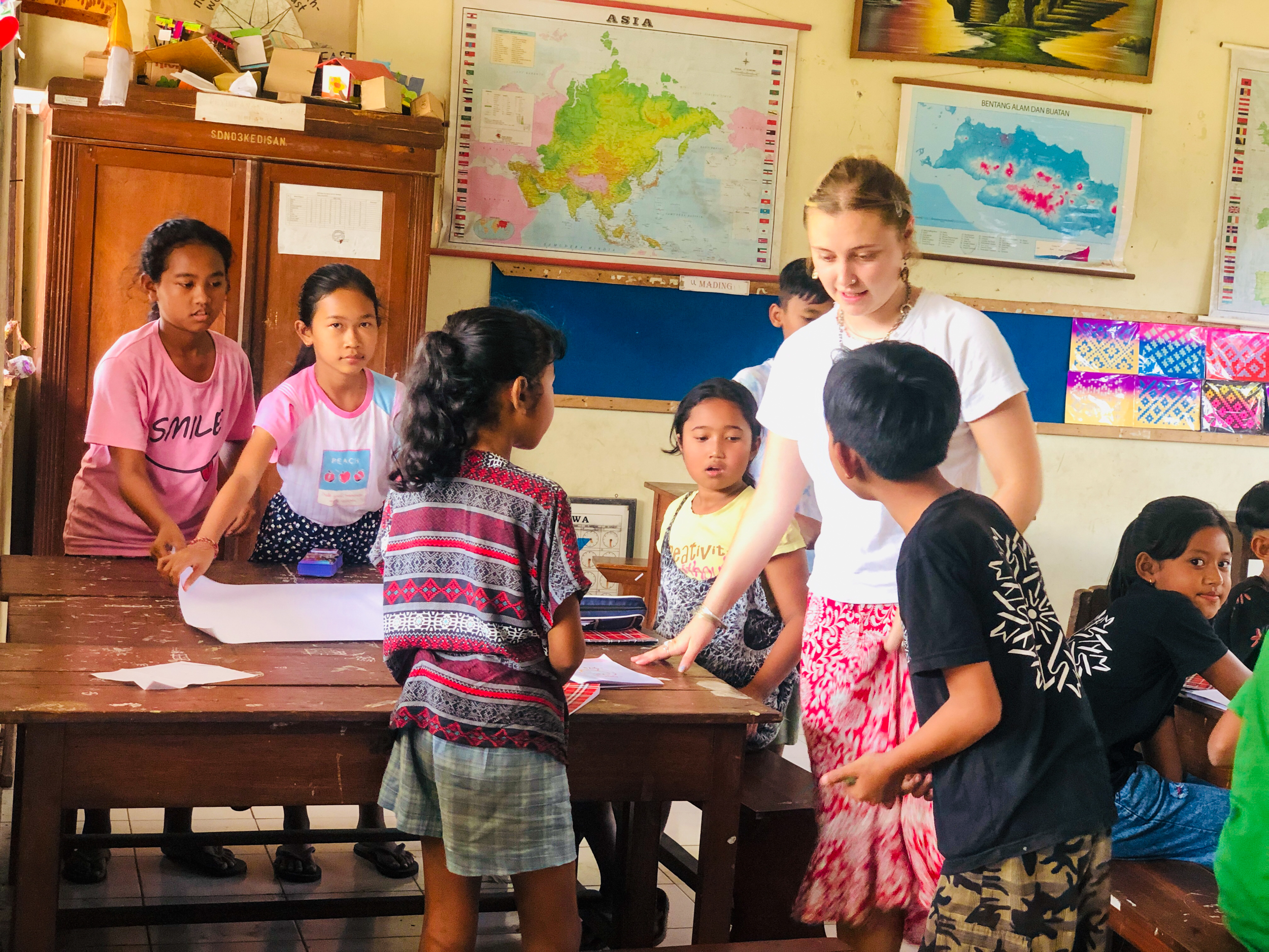 A female volunteer teaches a group of children in a bright classroom in Bali.
