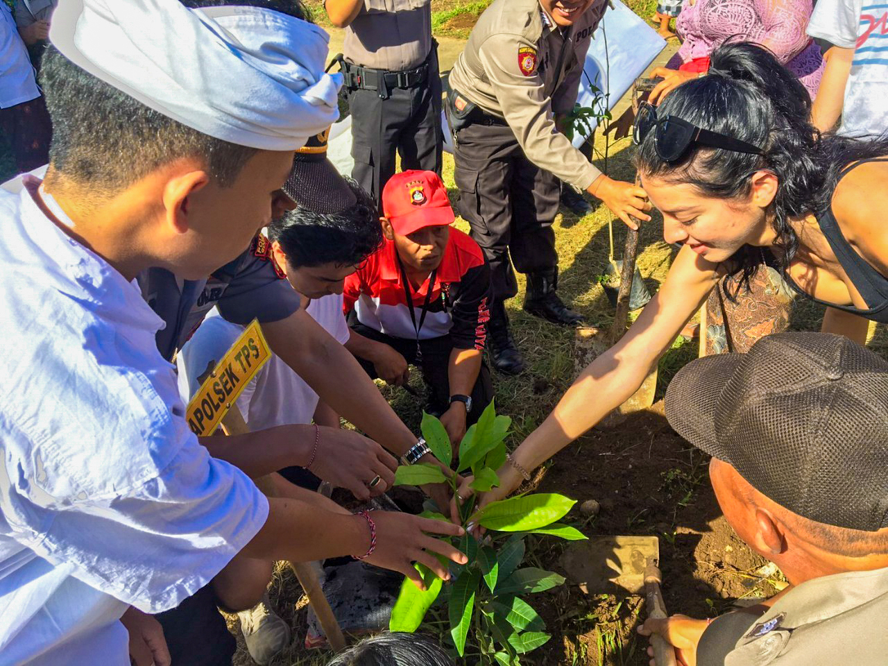 Diverse group of people collaboratively planting a young tree in the sunny soil of Bali.