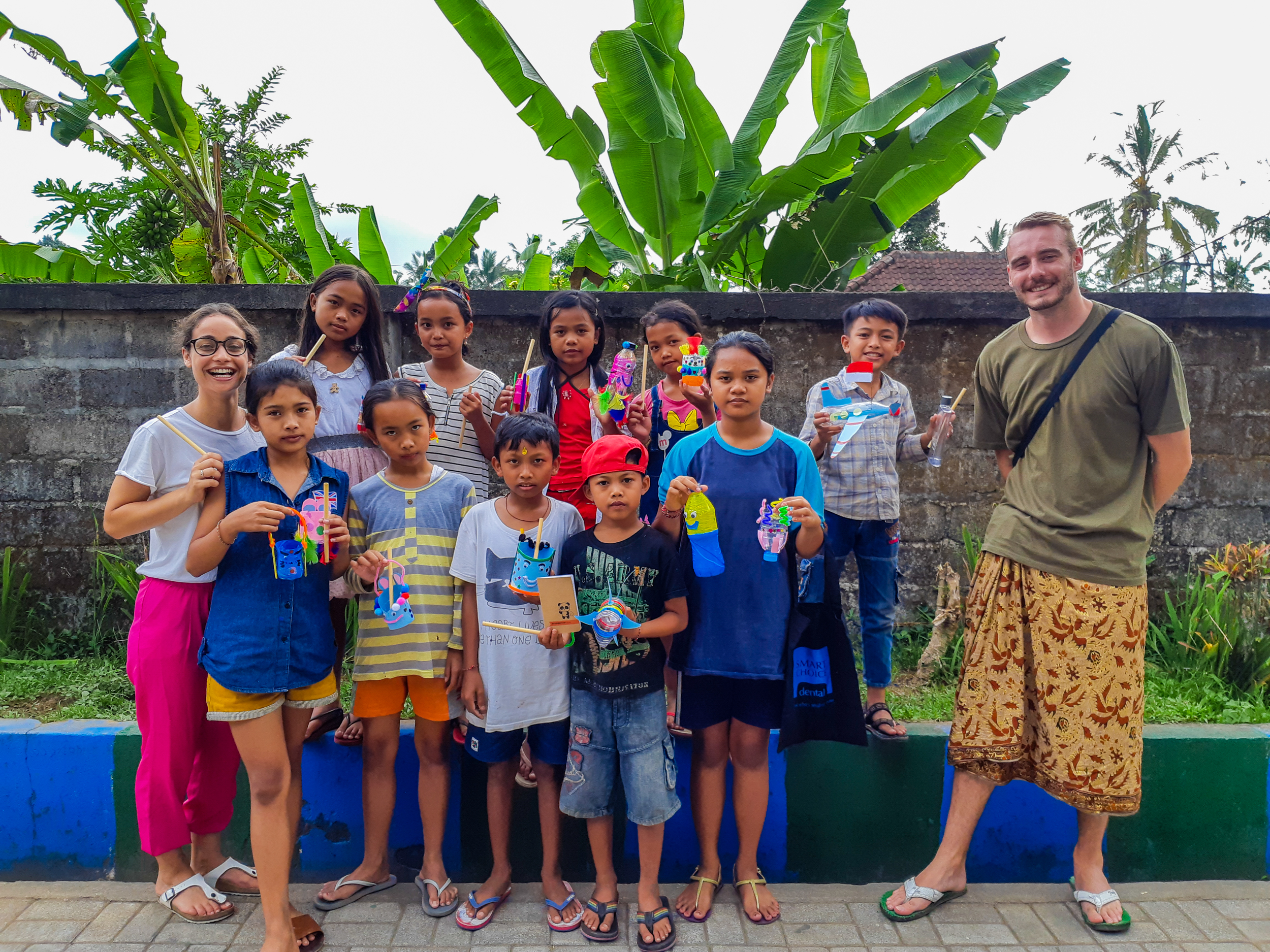 Smiling children and two adults proudly show off their colorful handmade crafts in Bali.