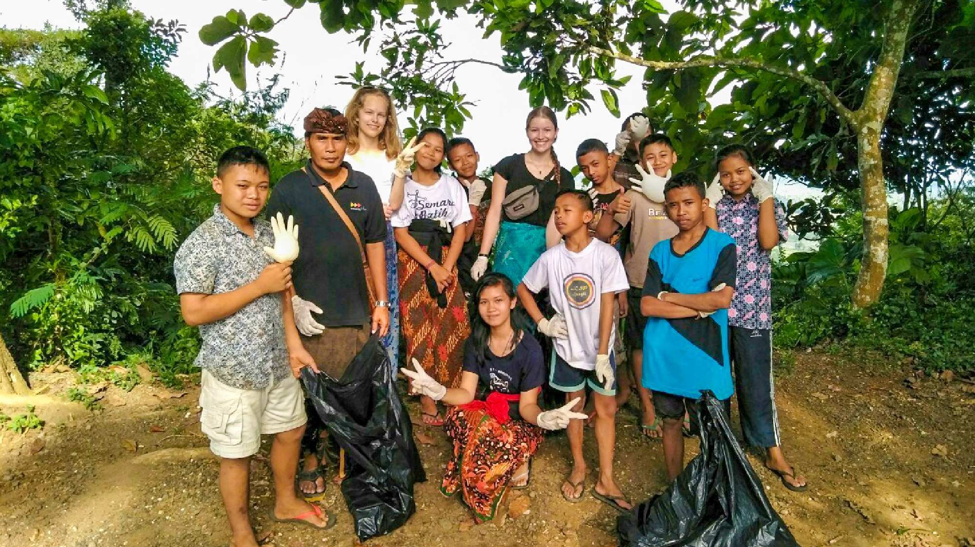 Smiling local children and volunteers holding trash bags after an environmental clean-up in Bali.