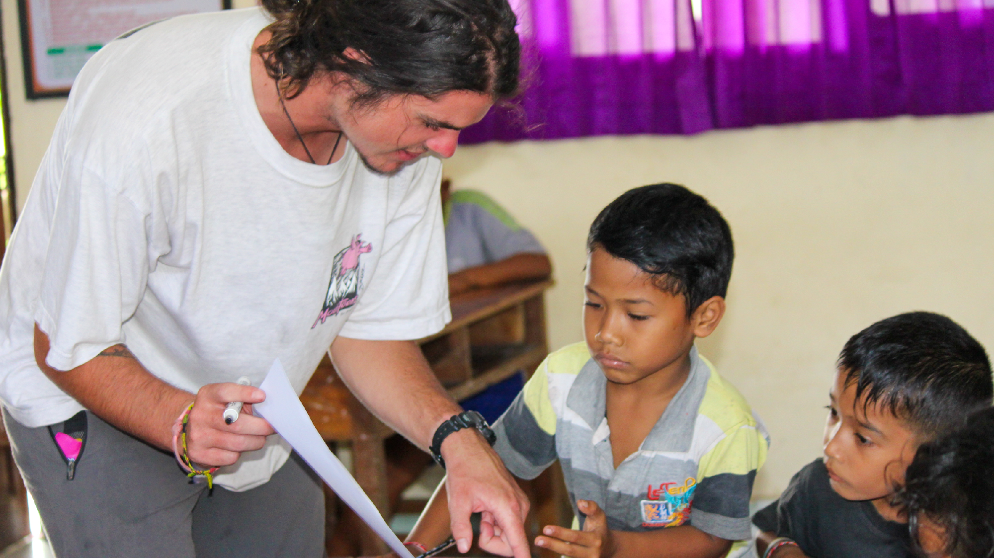 A volunteer teaches two young Balinese boys about environmental education in a classroom.