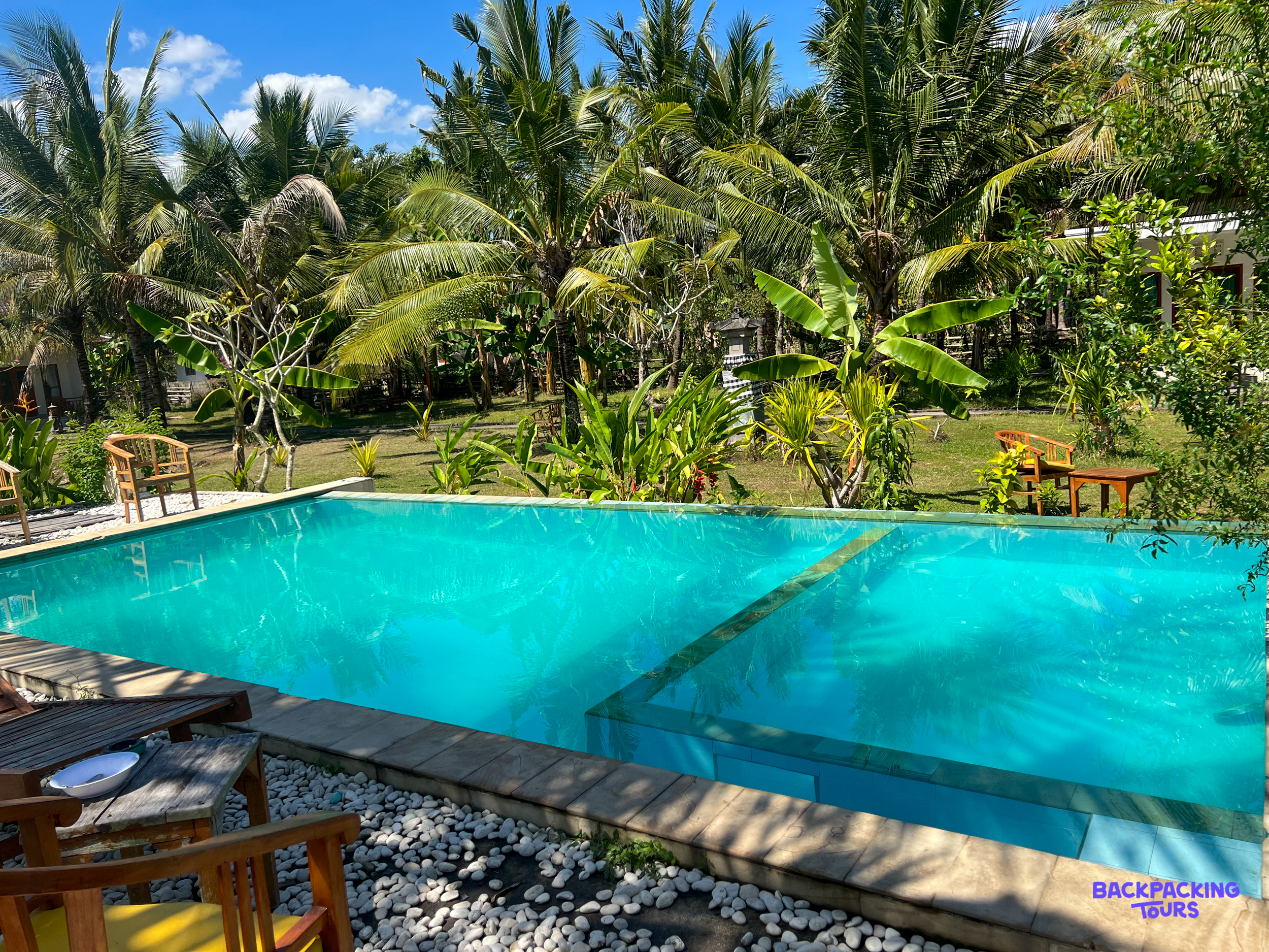 A serene swimming pool in Nusa Penida, framed by vibrant palm trees and lush tropical gardens.