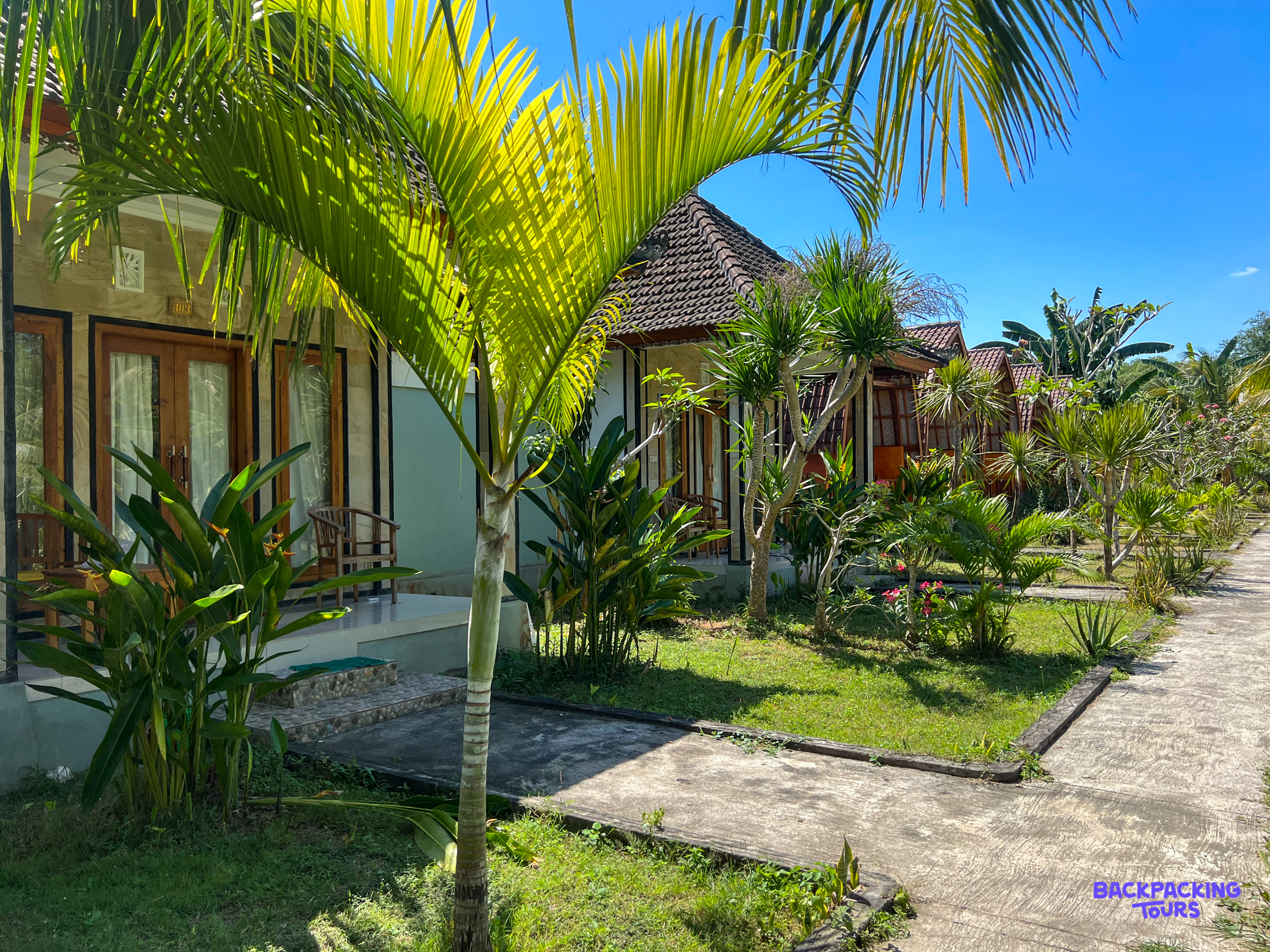 Tropical bungalows with lush gardens and palm trees under a sunny blue sky in Nusa Penida.