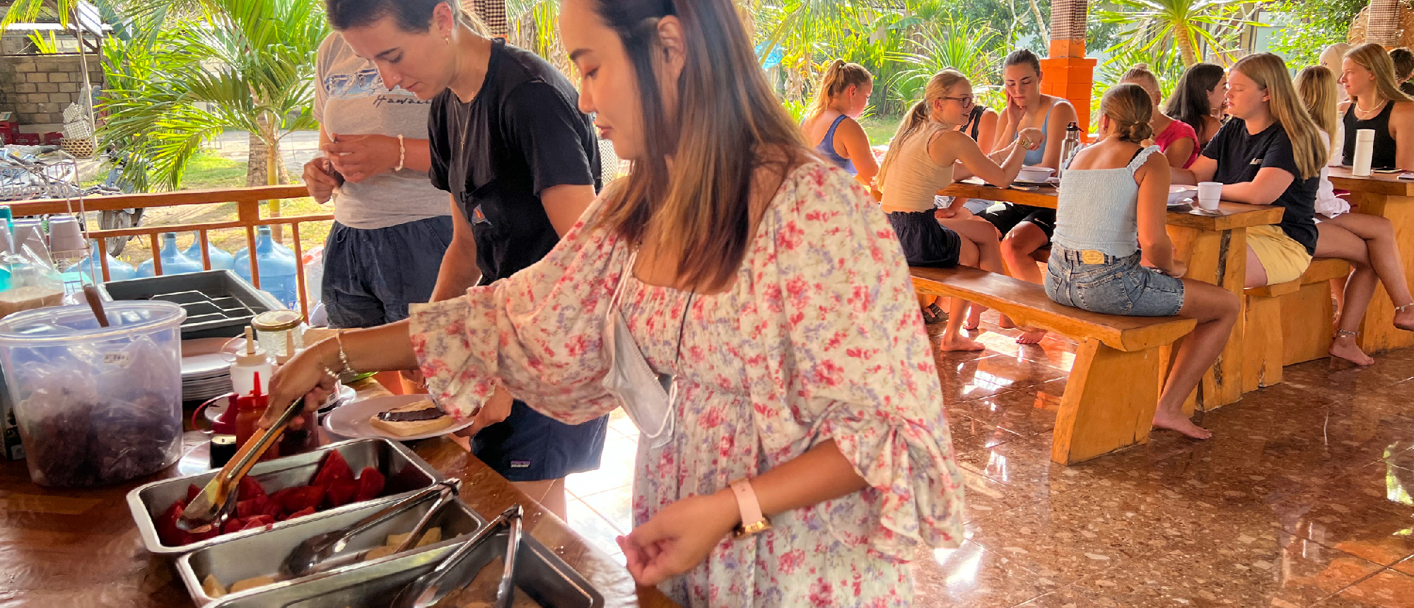 Young women serving themselves food and socializing at a casual outdoor dining area in Nusa Penida.