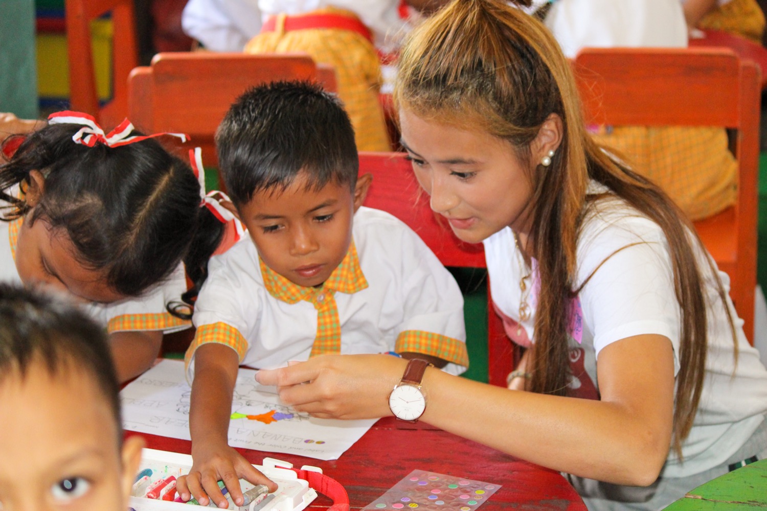 A female volunteer helps a young boy with his schoolwork at a kindergarten in Bali.