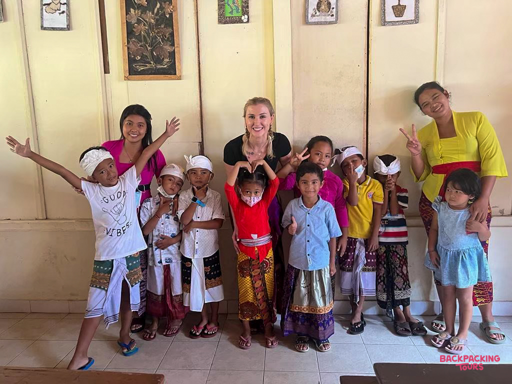 Happy Balinese children and local women smile with a volunteer inside a bright classroom.