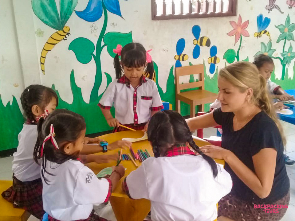 Young girls in Bali happily draw and color with a volunteer teacher in a vibrant kindergarten classroom.