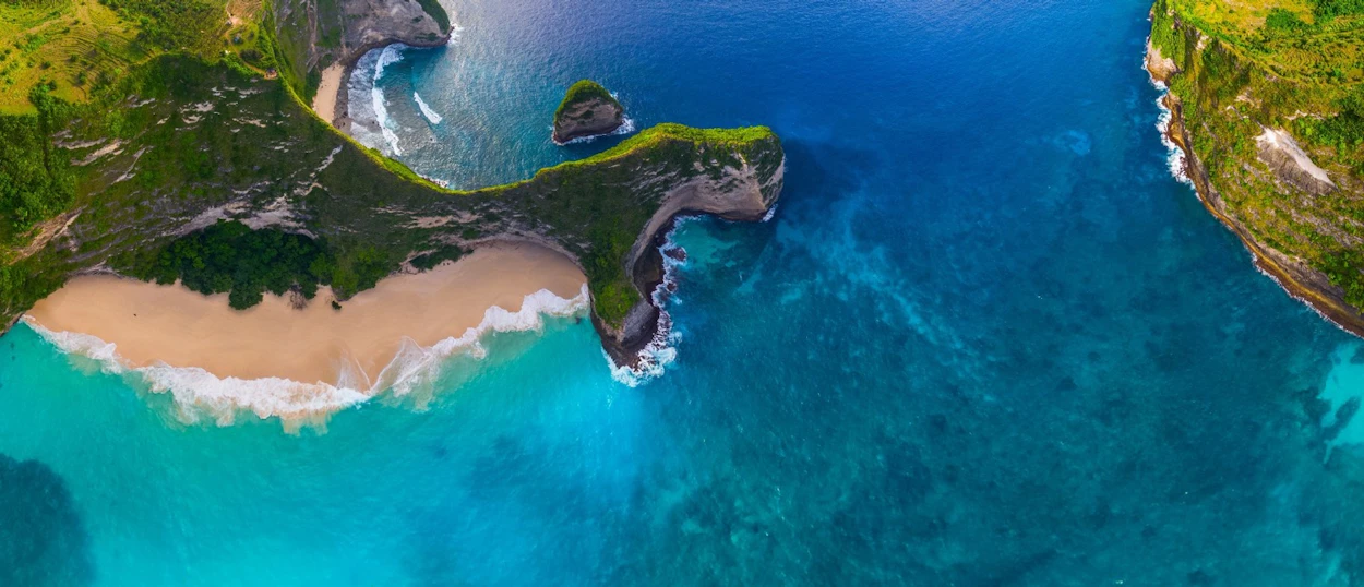 Stunning aerial view of Kelingking Beach, Nusa Penida, featuring a sandy beach and vibrant blue ocean.
