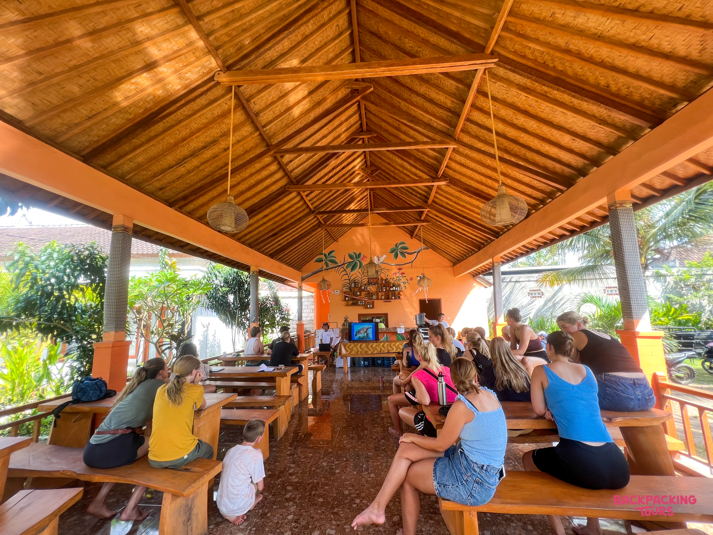 Travelers gather for an introductory briefing under a traditional wooden roof in Nusa Penida.