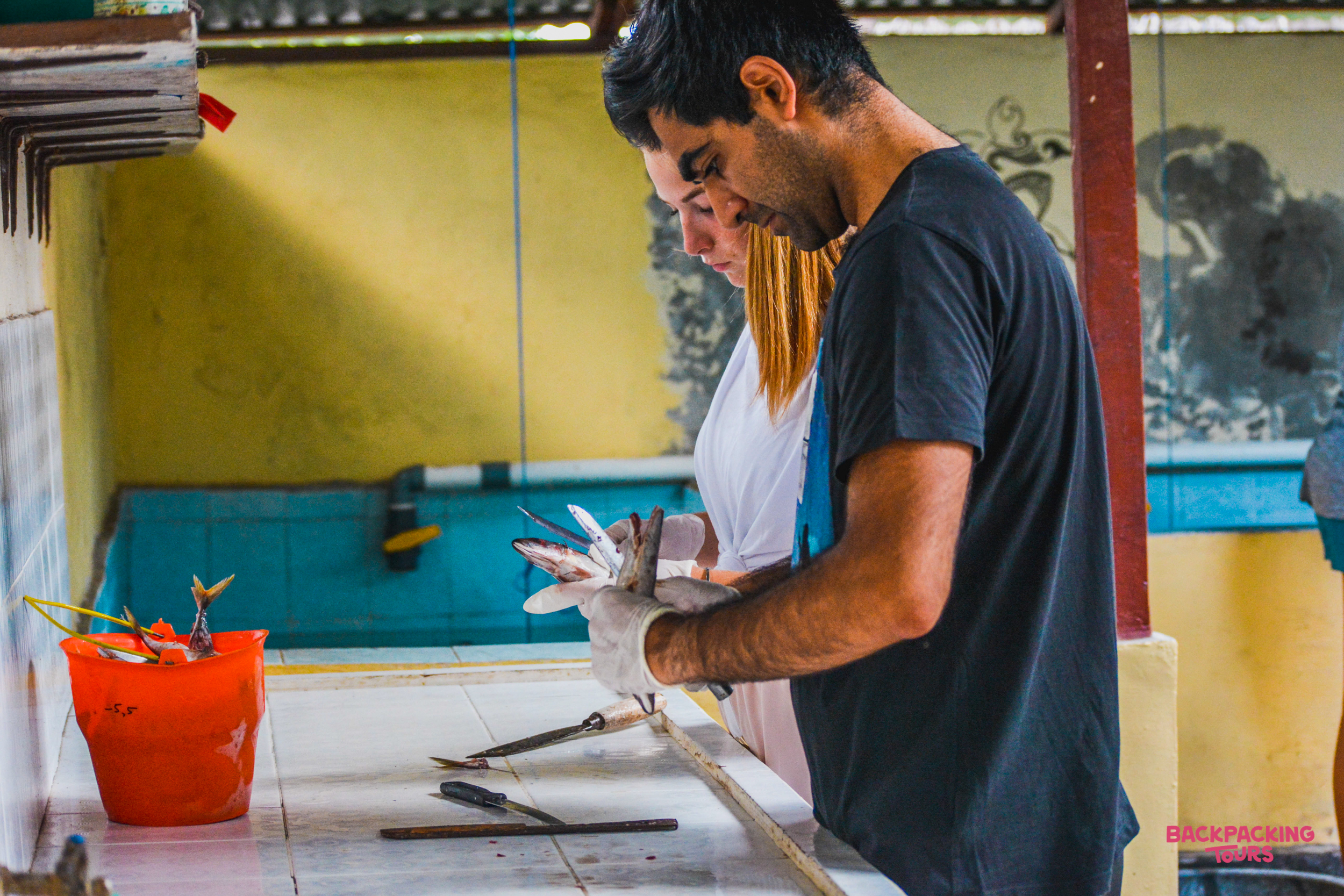 A man wearing gloves prepares fish on a tiled counter in Nusa Penida, Bali.