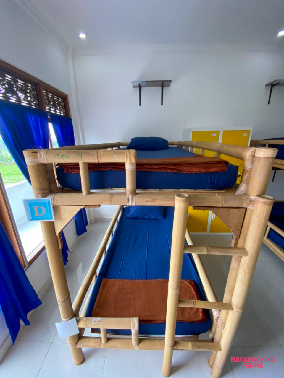 Clean and simple hostel accommodation with a bamboo bunk bed, blue mattresses, and yellow lockers.