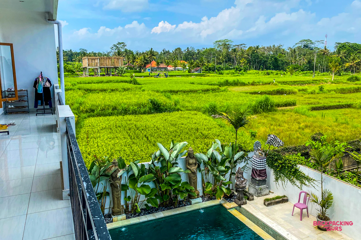 Balcony view of vibrant green rice paddies, a small pool, and traditional huts in Bali.
