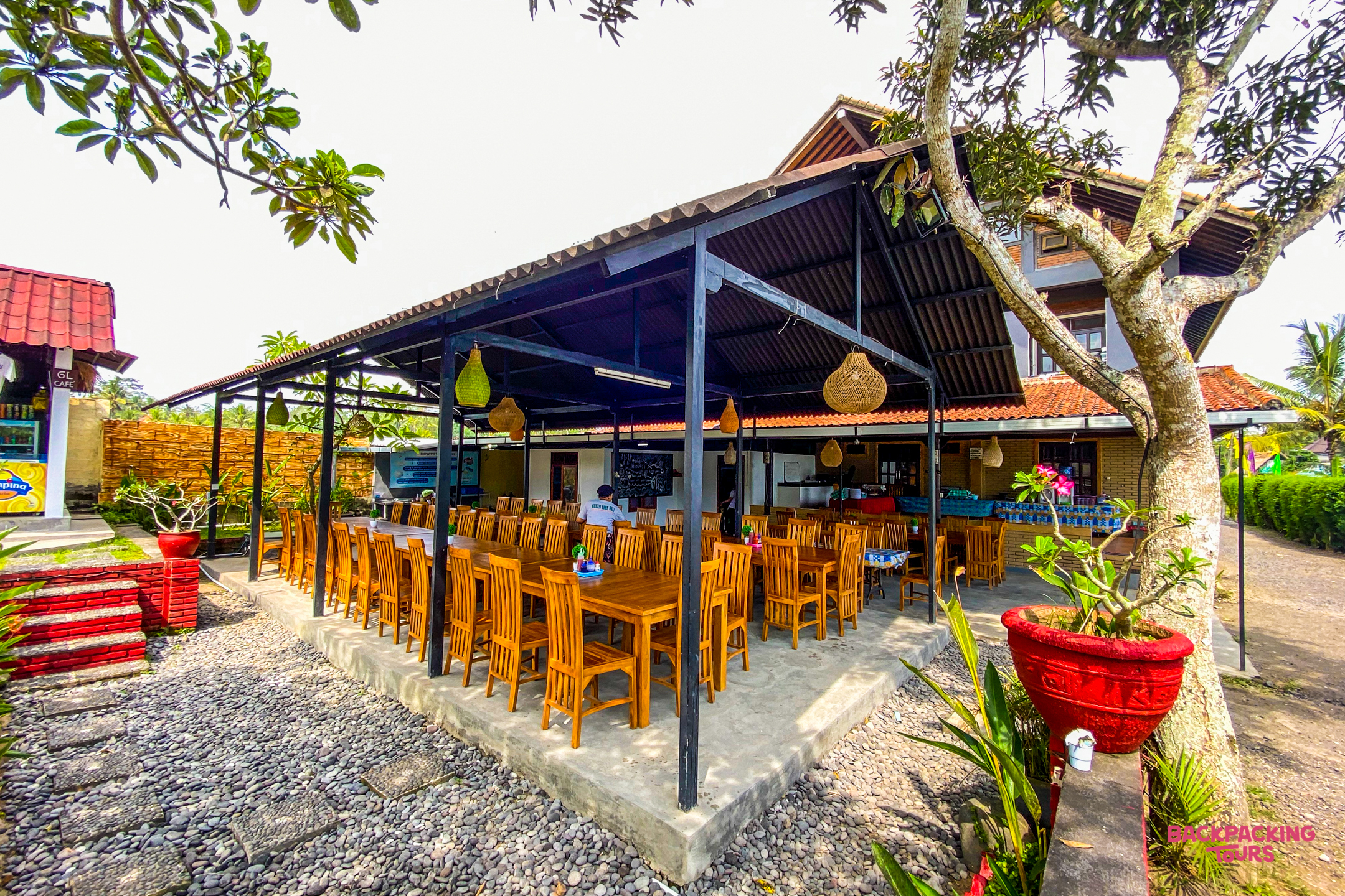 An inviting outdoor dining area with many wooden tables and chairs under a covered patio.