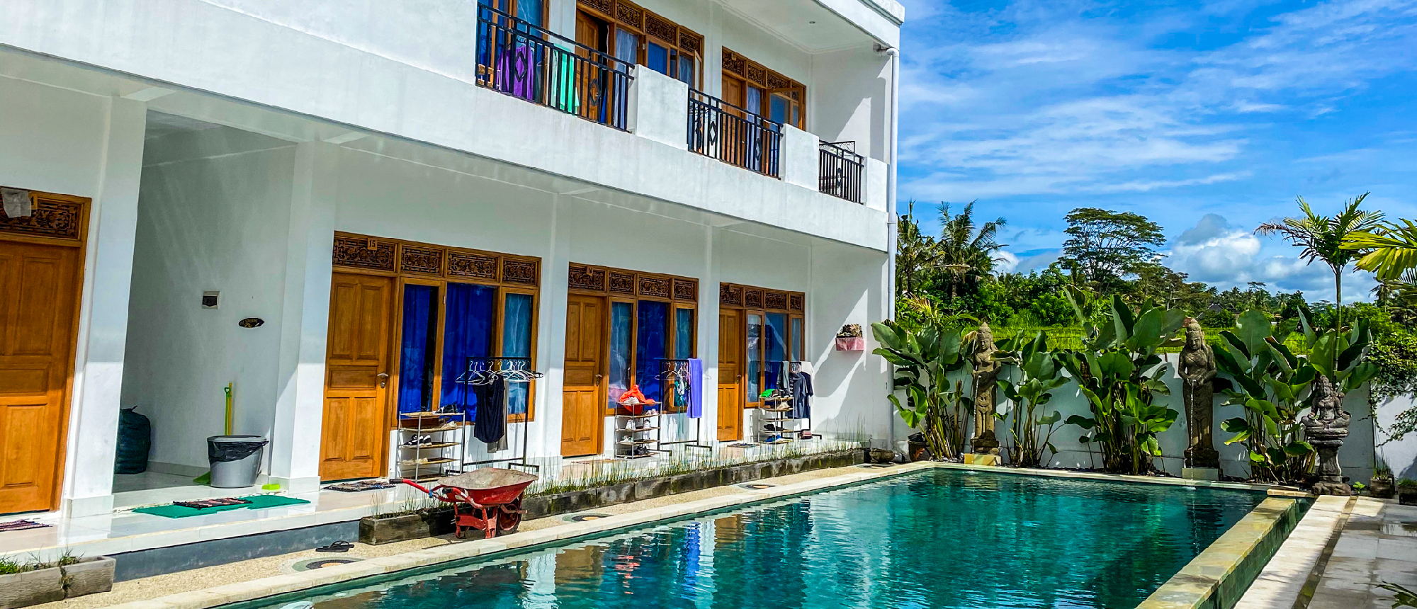 Modern white building with wooden doors and balconies next to a sparkling pool and tropical plants in Bali.