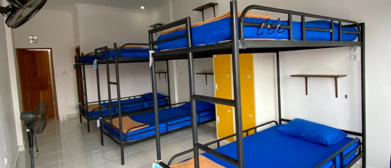 A clean and bright dormitory room with multiple bunk beds, blue mattresses, and yellow lockers.