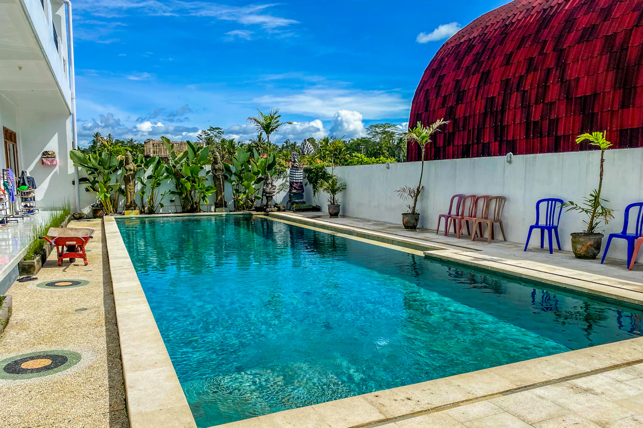 Bright blue swimming pool in a tropical Bali setting, with a red dome under a sunny sky.
