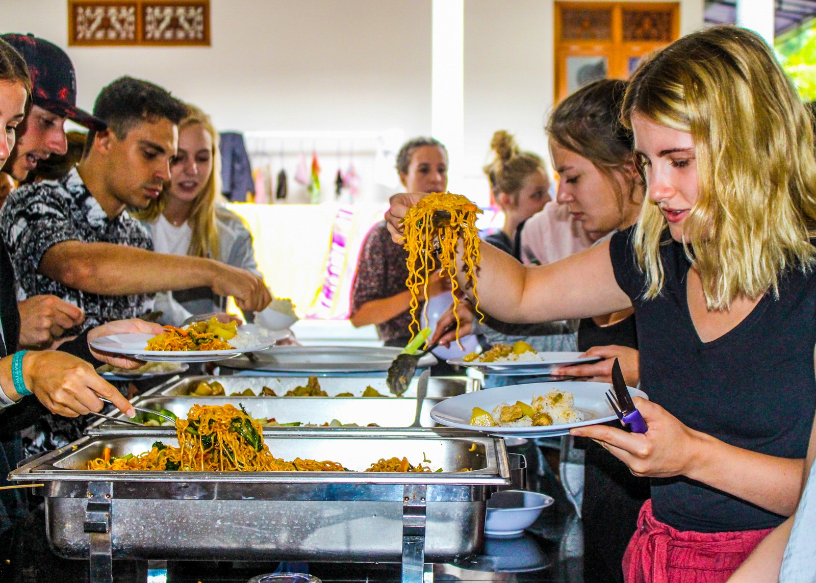 Young travelers happily serve themselves a buffet of local cuisine indoors from metal containers.