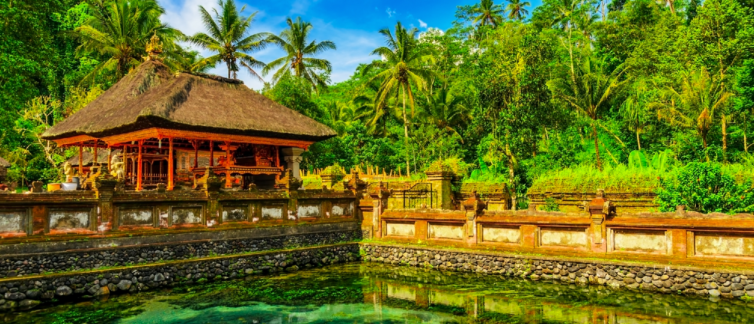 The sacred Tirta Empul temple in Bali, featuring a traditional thatched roof and serene water pool.