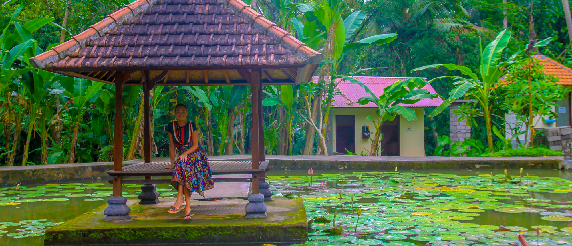 Woman relaxing in a traditional gazebo over a lily pond amidst lush greenery in Ubud, Bali.