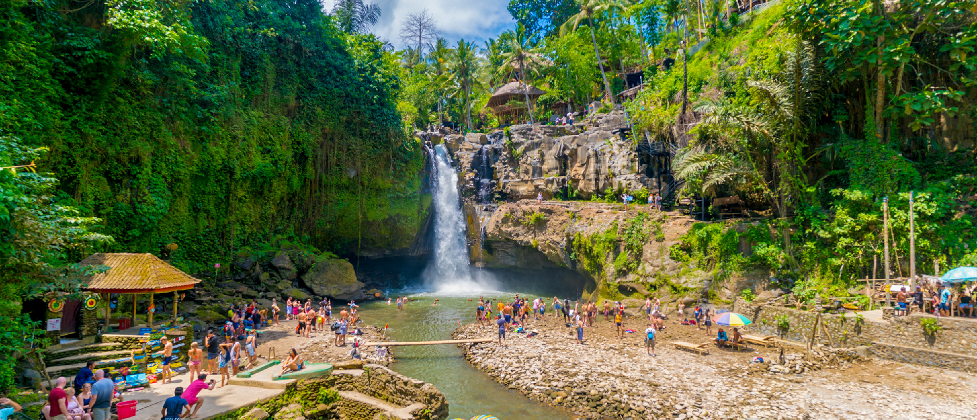 Many people swim and gather at the base of Tegenungan Waterfall amidst lush Balinese jungle.