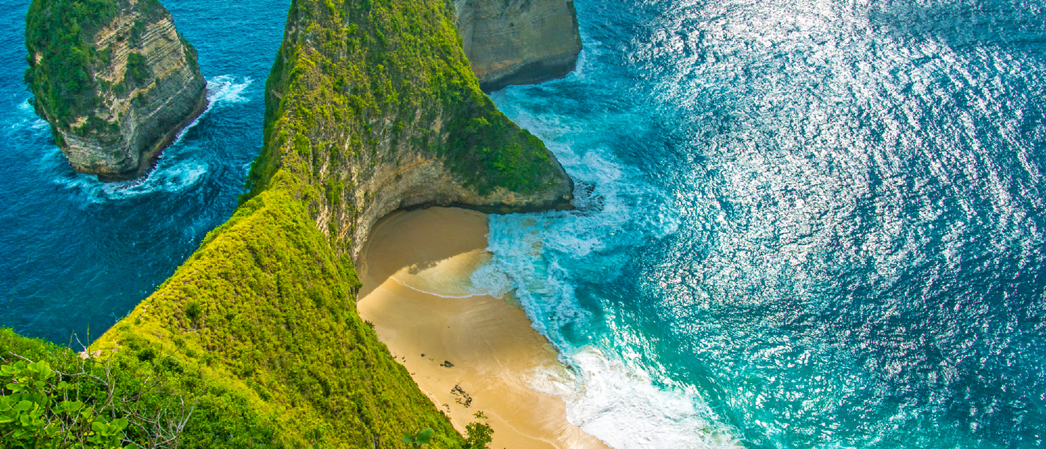 Majestic green cliffs overlook a secluded sandy beach with crashing turquoise waves in Bali.