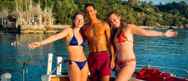 Three smiling friends in swimsuits on a boat during an island-hopping trip near Paraty, Brazil.