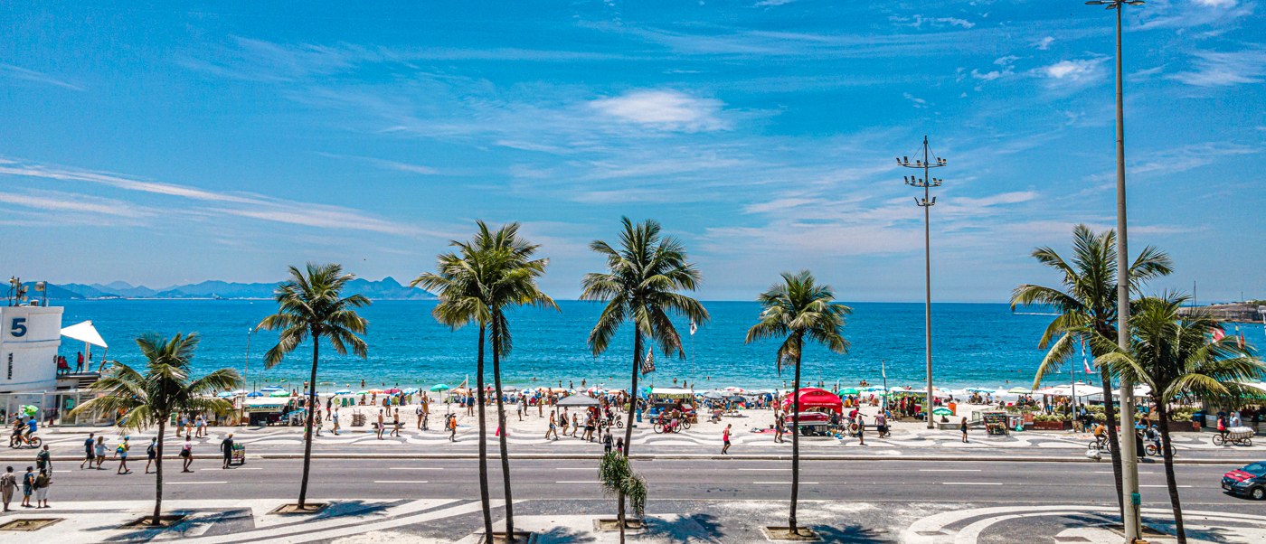Palm trees line the busy Copacabana Beach in Rio de Janeiro with people enjoying the sunny day.