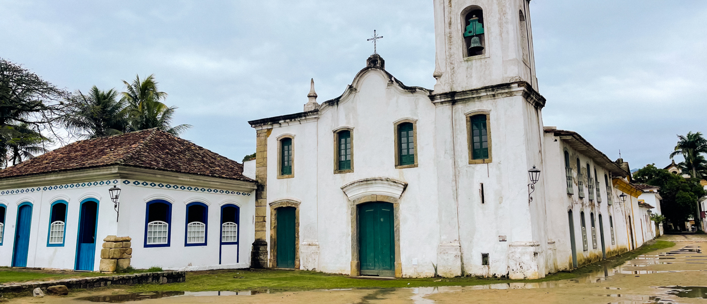 A historic white church and colonial buildings with blue and green doors in Paraty, Brazil.