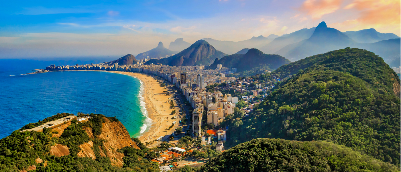 Panoramic view of Rio de Janeiro's curving beach, vibrant blue ocean, city, and lush green mountains.