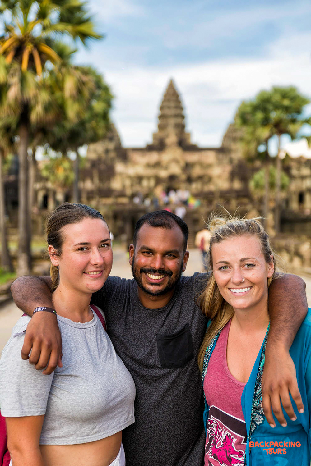 Three happy travelers and their guide smiling in front of the majestic Angkor Wat temple.