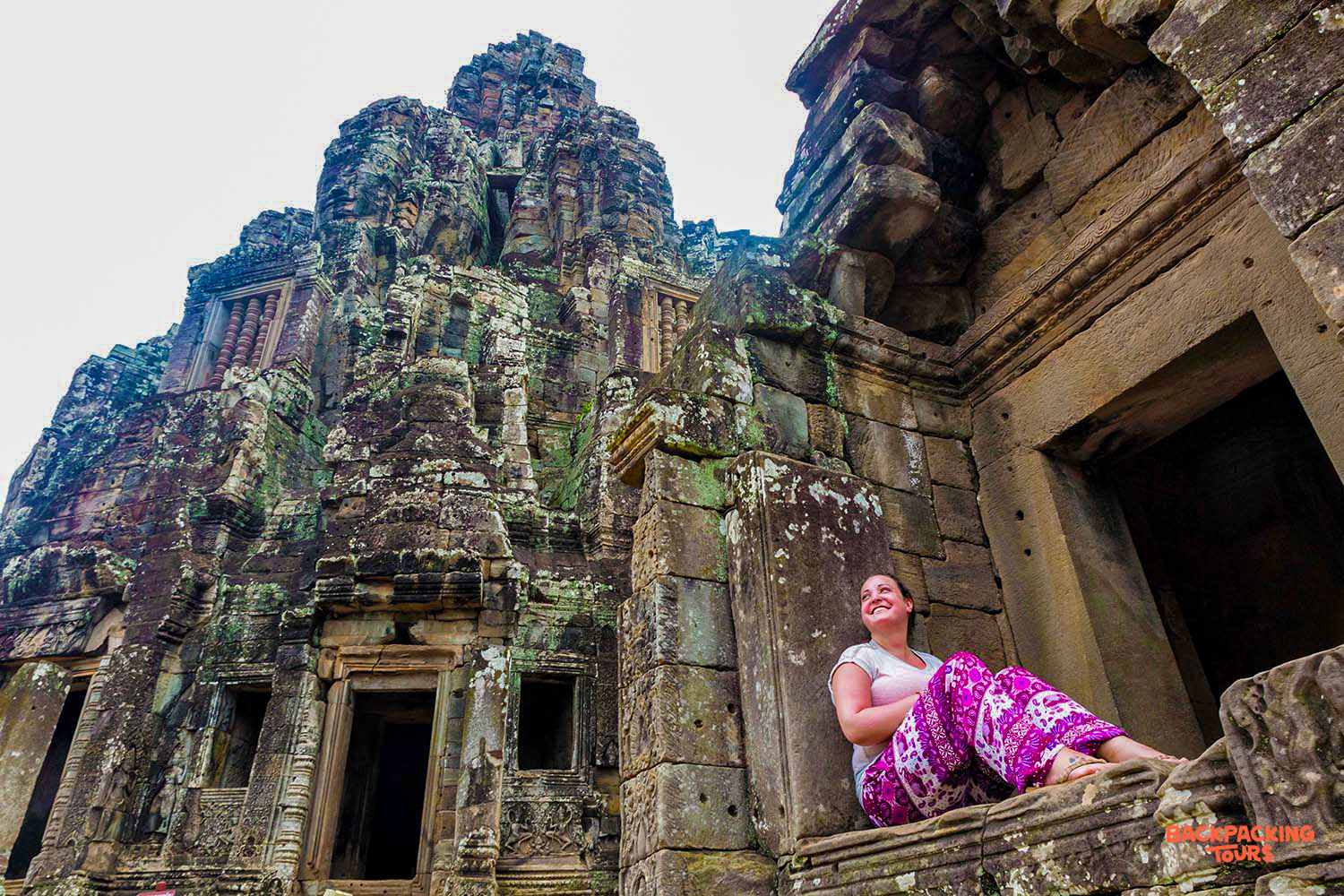 Traveler smiles, resting on ancient stone architecture at the magnificent Angkor Wat temple.